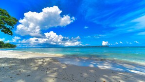 A beach with clear turquoise water, white sand, and a large cloud in the sky. - Sea Shell Samssara (Port Blair)