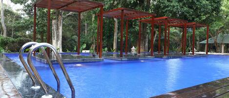 A swimming pool with a wooden deck and metal railings, surrounded by lush greenery.