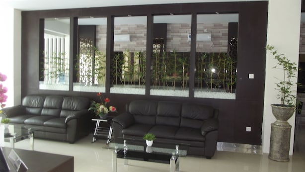 A modern living room with two dark leather sofas, a glass coffee table, and a large window with a view of bamboo plants. - Manado Inn Hotel (Manado)