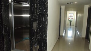 A modern hallway with a marble wall, a trash bin, and an elevator. - Manado Inn Hotel (Manado)