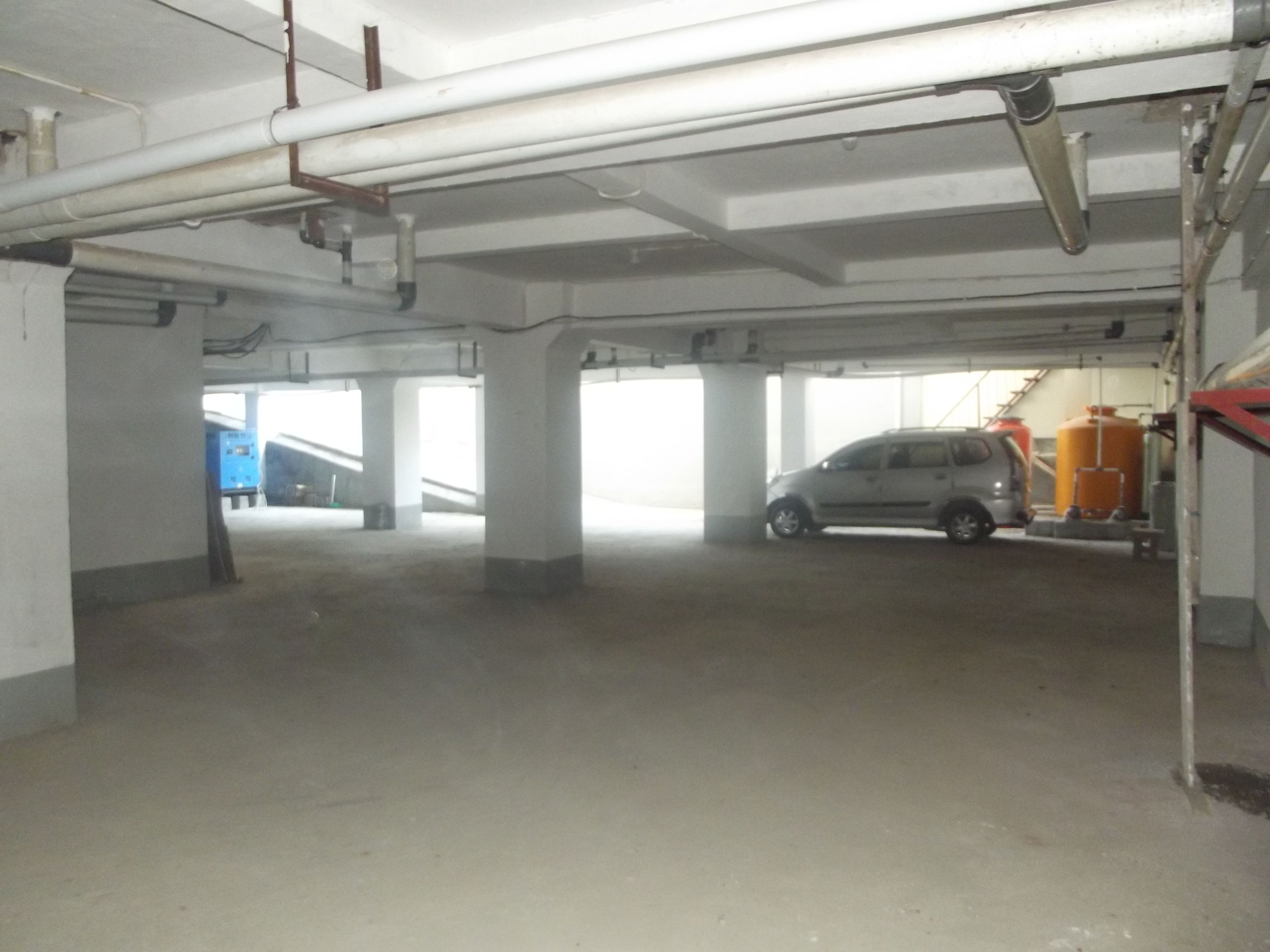 A parking garage with concrete pillars, a car, and industrial equipment.