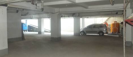 A parking garage with concrete pillars, a car, and industrial equipment.