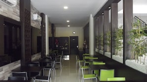 A modern indoor dining area with tables and chairs, a staircase, and decorative plants. - Manado Inn Hotel (Manado)