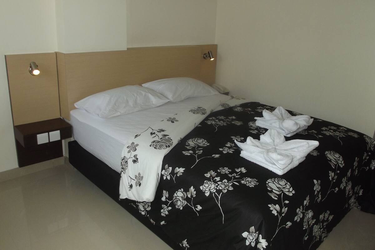 A neatly made bed with a black and white floral bedspread and white pillows.