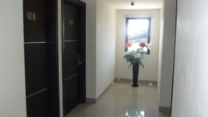 A hallway with two doors labeled 108 and 107, a potted plant with flowers, and a window with blinds. - Manado Inn Hotel (Manado)