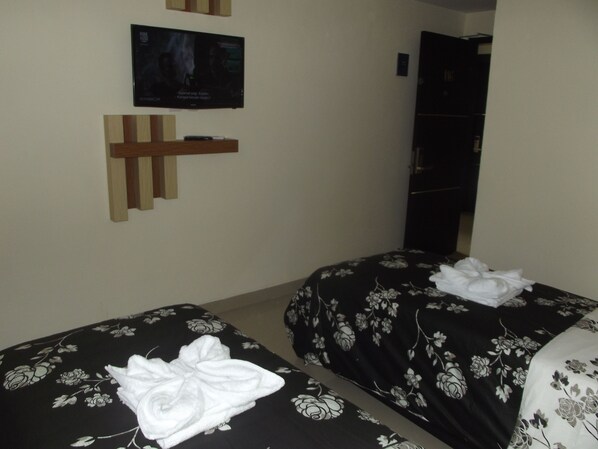 Habitación de hotel con dos camas, un televisor en la pared y un estante de madera.