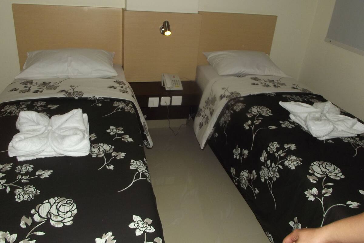 A hotel room with two beds, each with a floral bedspread and a white pillow. There is a nightstand with a phone and a lamp between the beds.