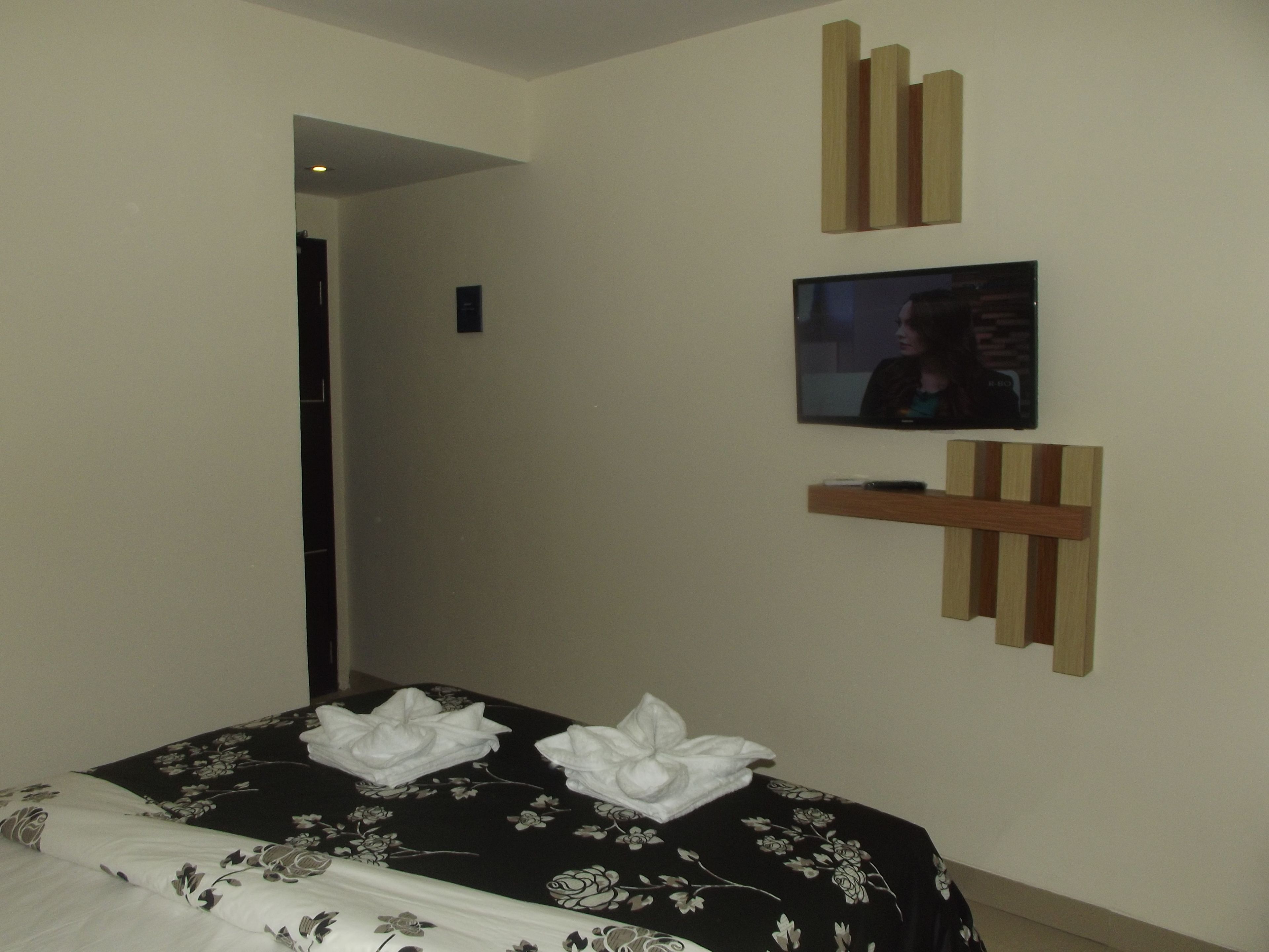 Una habitación de hotel con una cama, un televisor montado en la pared y un estante de madera.