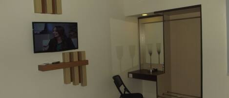 Una habitación de hotel con cama, televisor montado en la pared, espejo y armario.