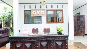 A reception desk with a sign reading "OYO" above it, two chairs, a potted plant, and a decorative wooden panel. - Hotel O Loesje Guest House Syariah (Malang)