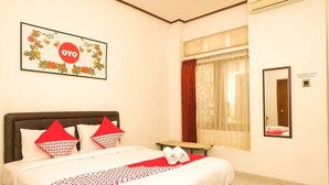 A hotel room with a bed, a bedside table, a mirror, a window with curtains, and a wall-mounted sign. - Hotel O Loesje Guest House Syariah (Malang)