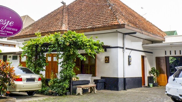 A guest house with a tiled roof, a wooden bench, and a car parked in front. - Hotel O Loesje Guest House Syariah (Malang)