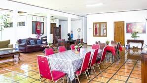A spacious dining area with a large table, red chairs, and a patterned tablecloth. There is a sofa and a wooden cabinet in the background. - Hotel O Loesje Guest House Syariah (Malang)