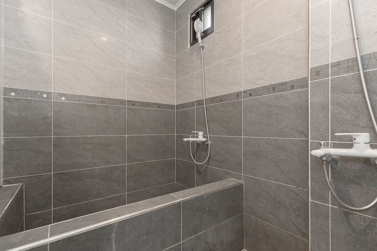 Un espacio de ducha con azulejos grises, un cabezal de ducha manual y un grifo empotrado en la pared.