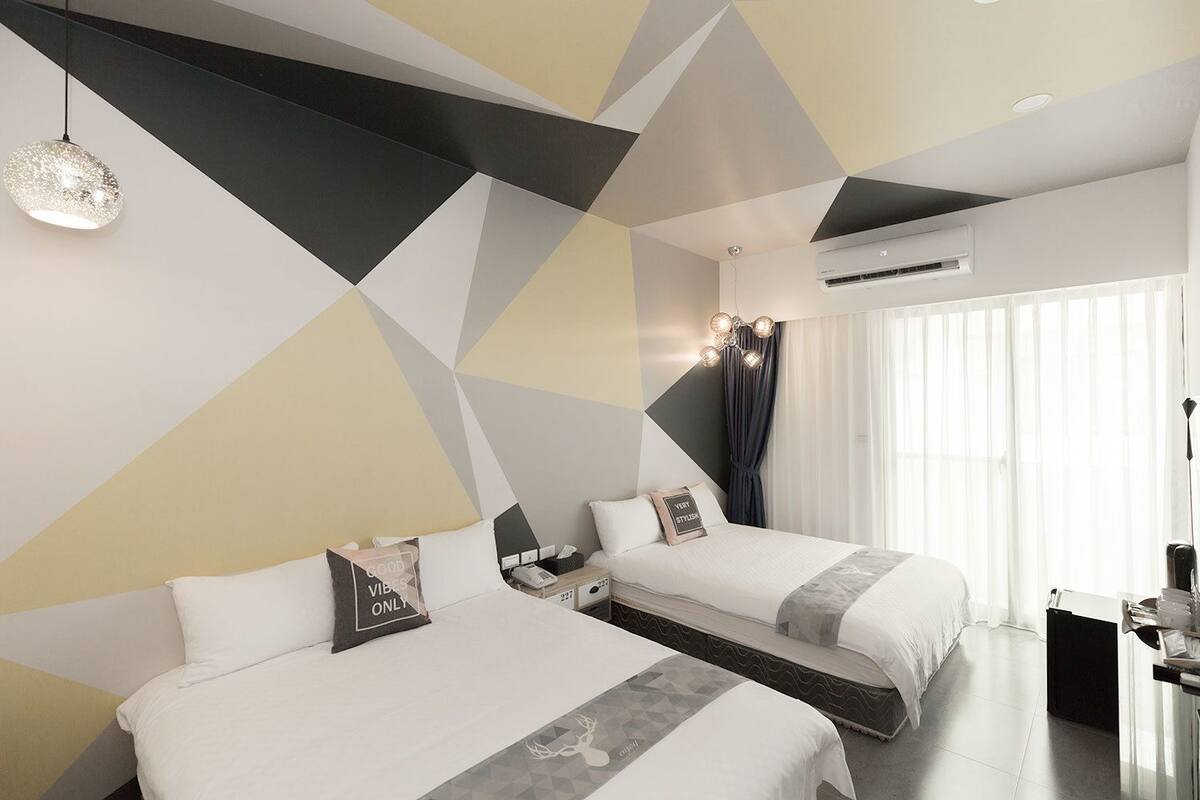 A modern hotel room with two beds, a desk, and a large window with curtains.