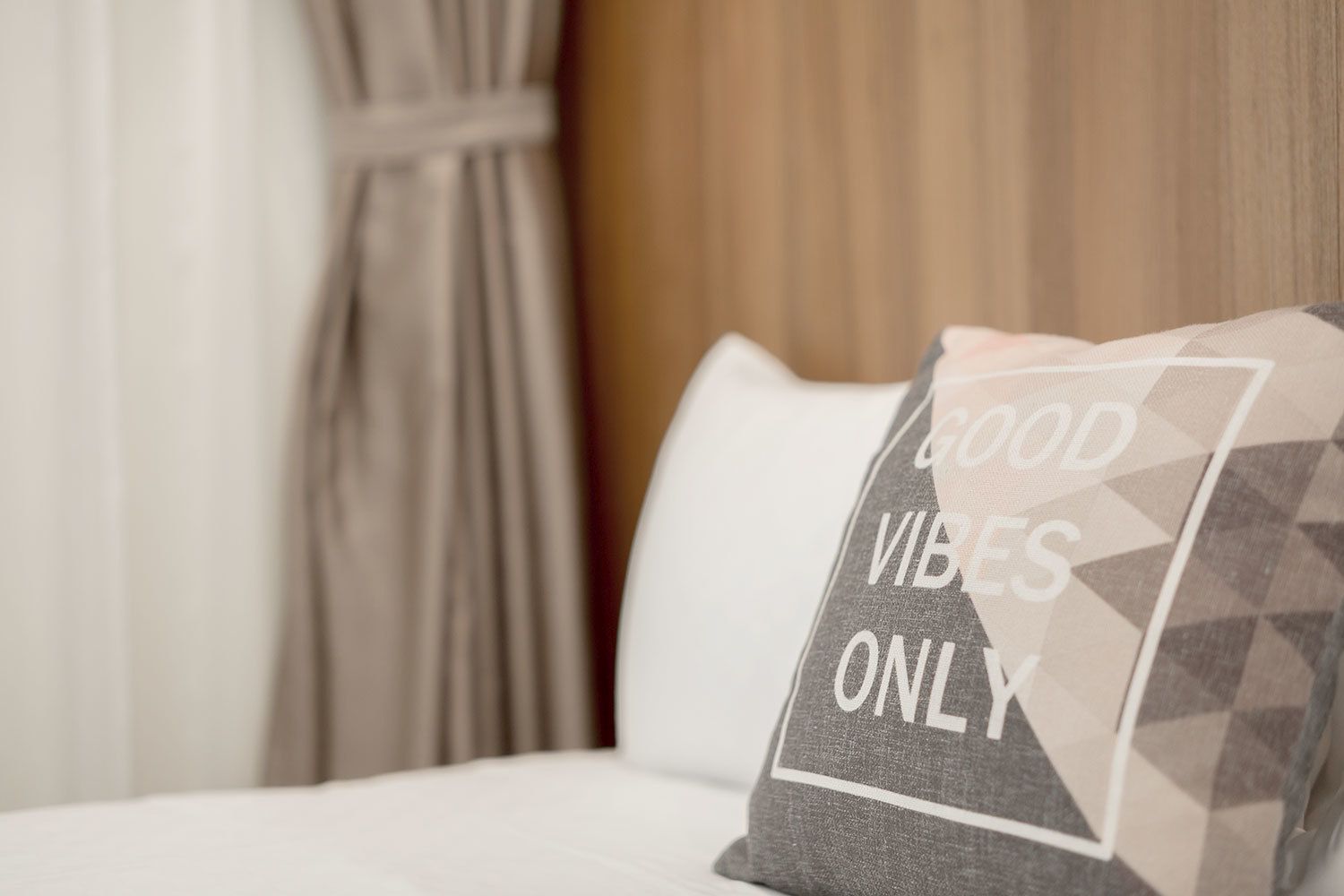 Un lit avec un oreiller sur lequel on peut lire « SEULEMENT LES BONNES VIBES » et un rideau en arrière-plan.