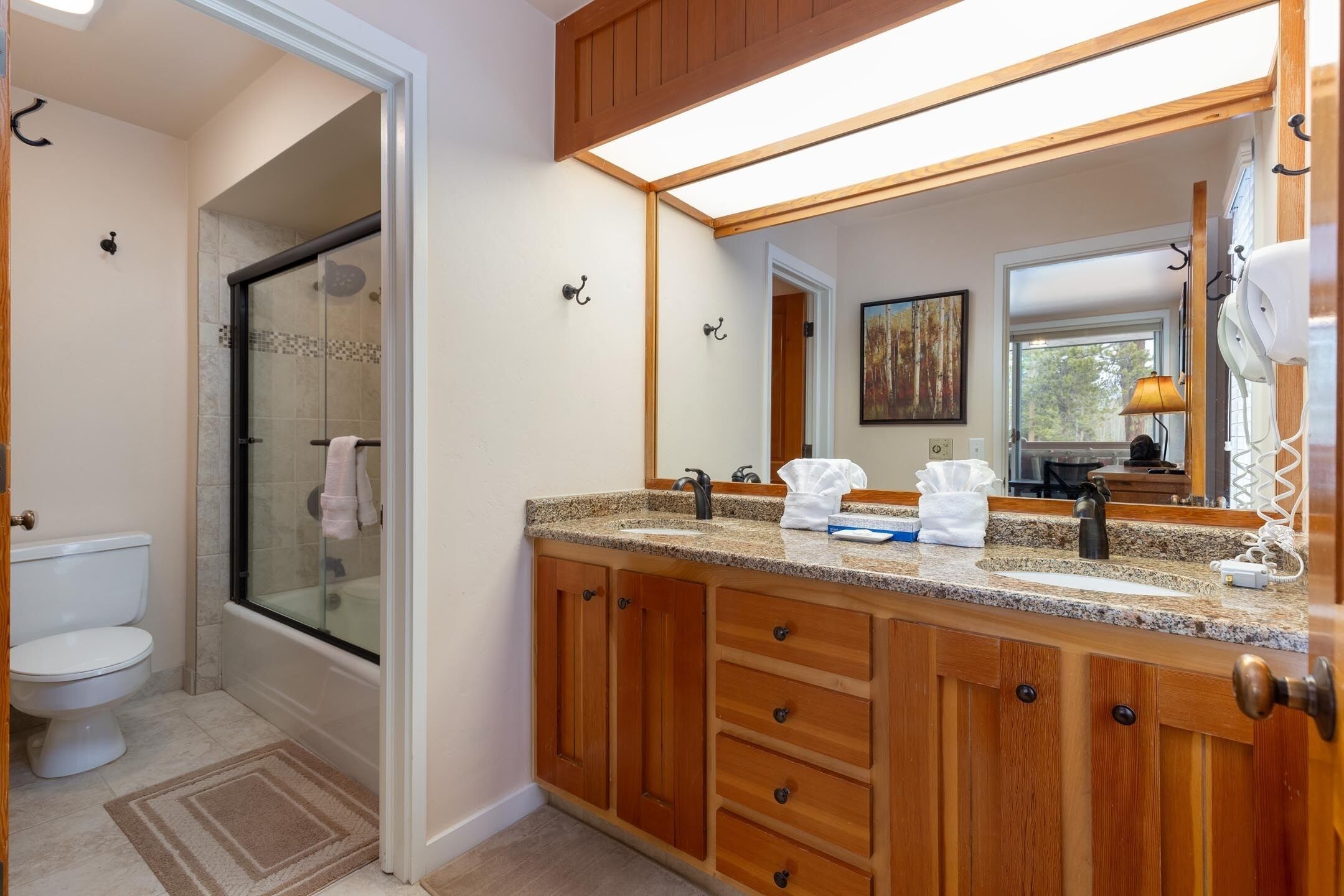 A bathroom with a glass shower enclosure, a white toilet, wooden cabinets, a granite countertop, and a large mirror.