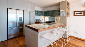 A modern kitchen with stainless steel appliances, a wooden island with bar stools, and a view of the city through the window.