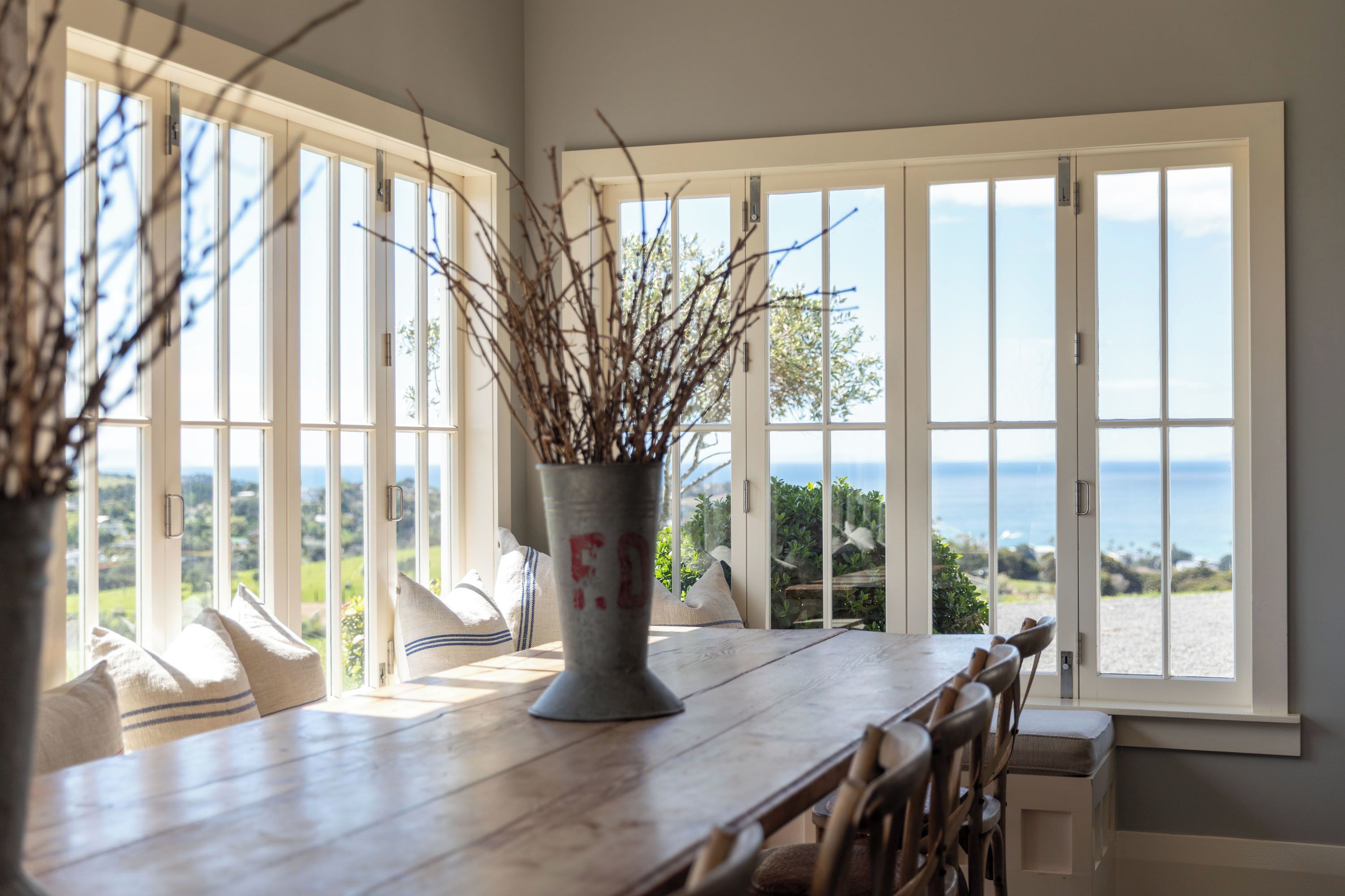 Un coin repas avec une table en bois, des chaises et un vase décoré de branches.