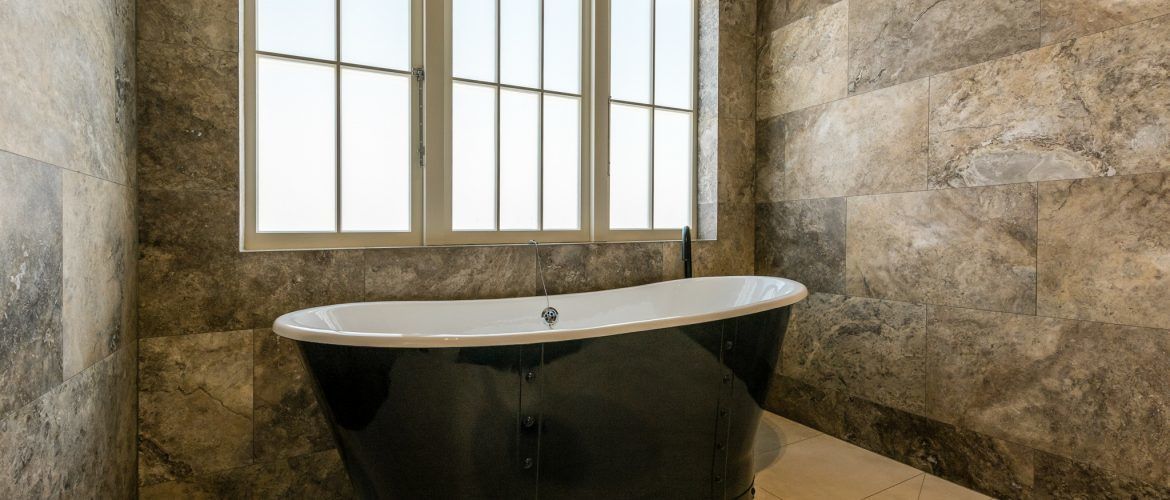 Un baño moderno con una bañera independiente, ventanas amplias y paredes de piedra.