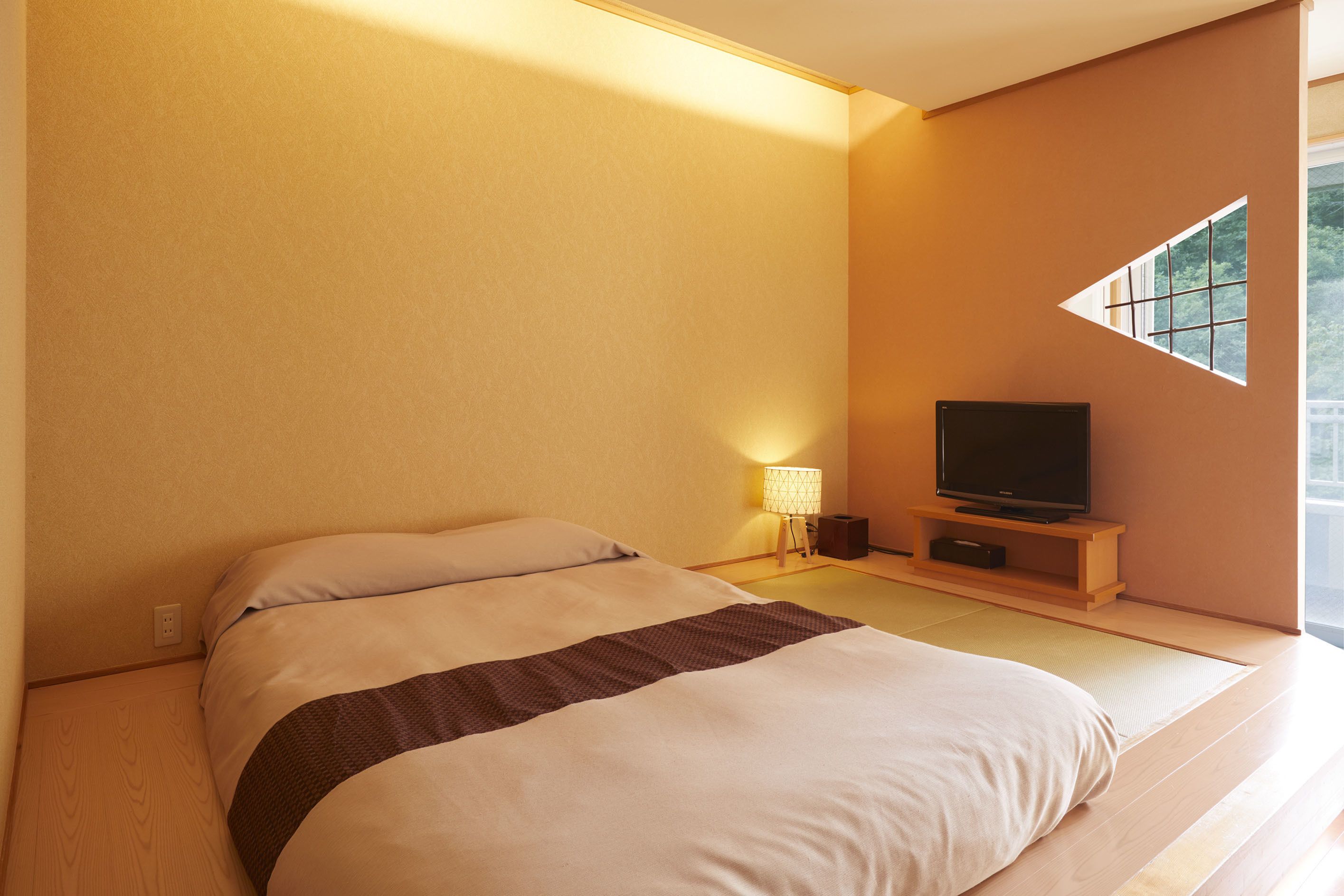 A bedroom with a bed, a television on a stand, and a window.