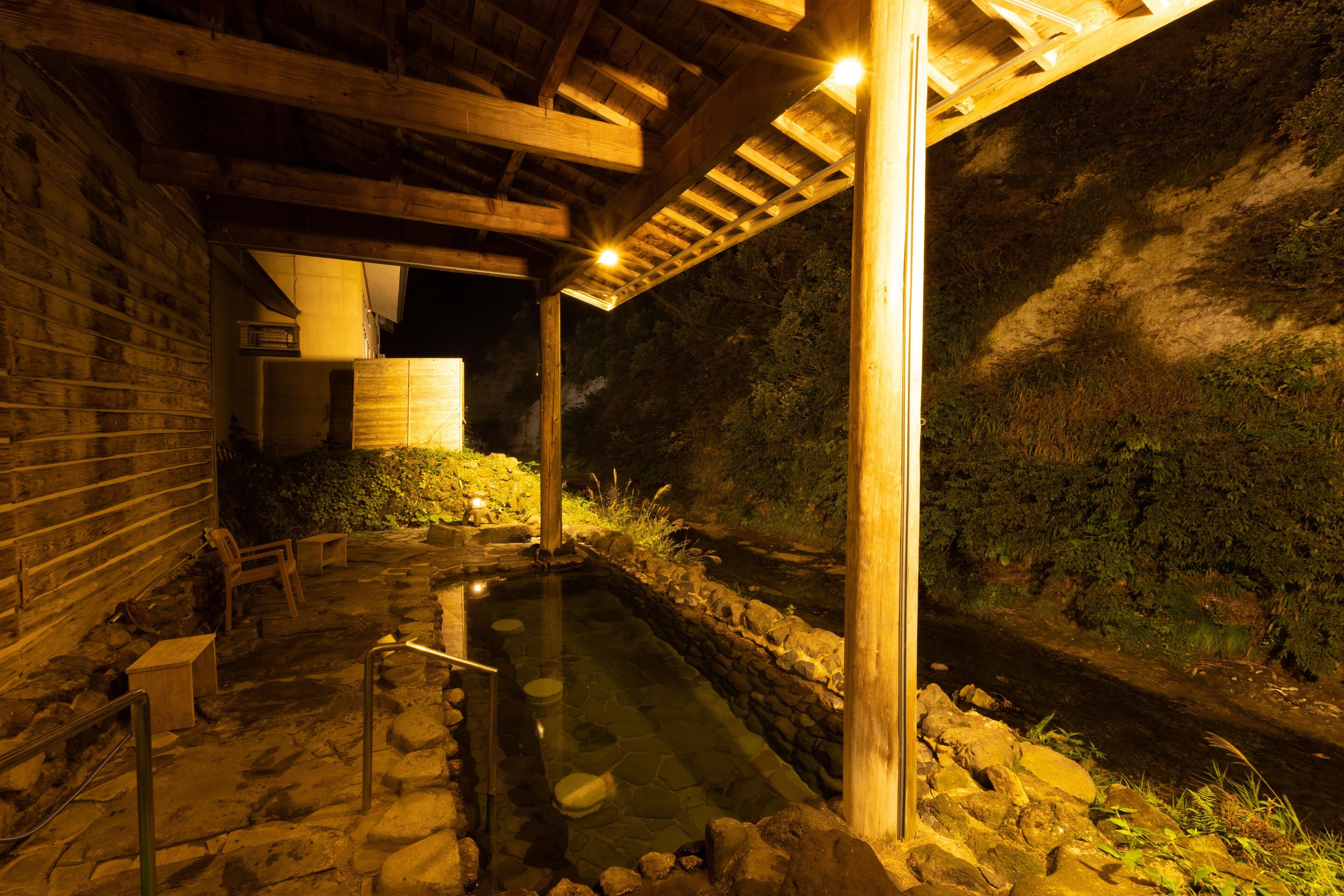 A stone hot spring area with wooden benches and a wooden pergola structure.