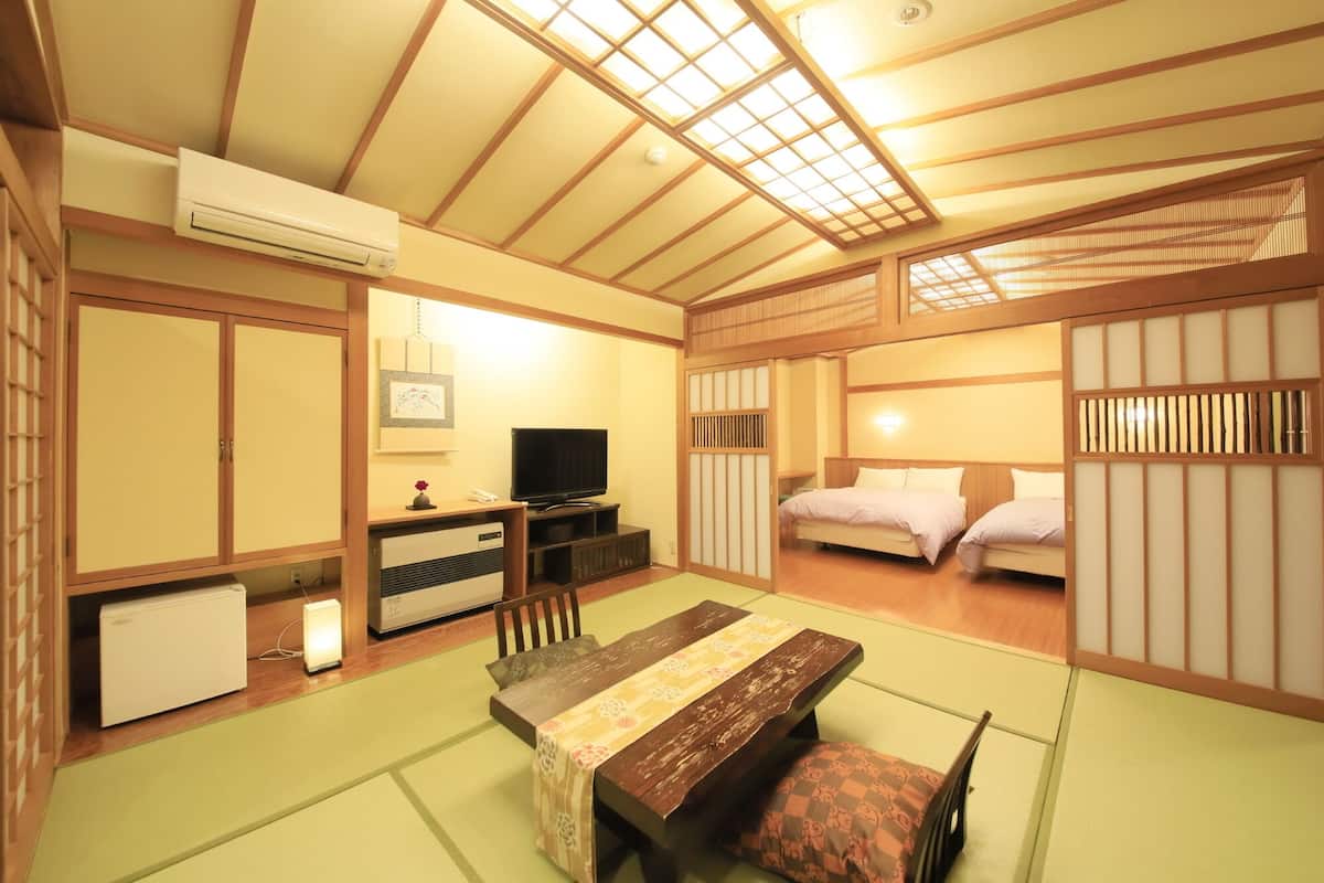 Ett traditionellt japanskt rum med tatamimattor på golvet, ett lågt bord, en säng och skjutdörrar.