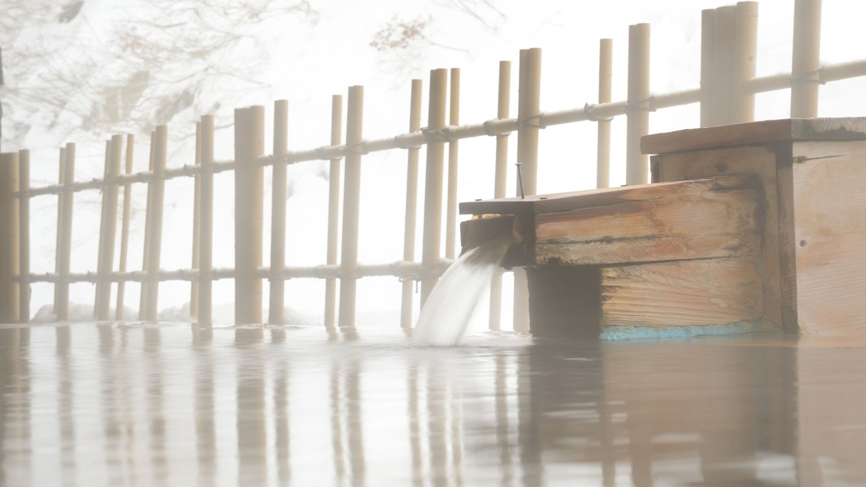 A wooden fence with vertical slats and a wooden structure with a faucet.