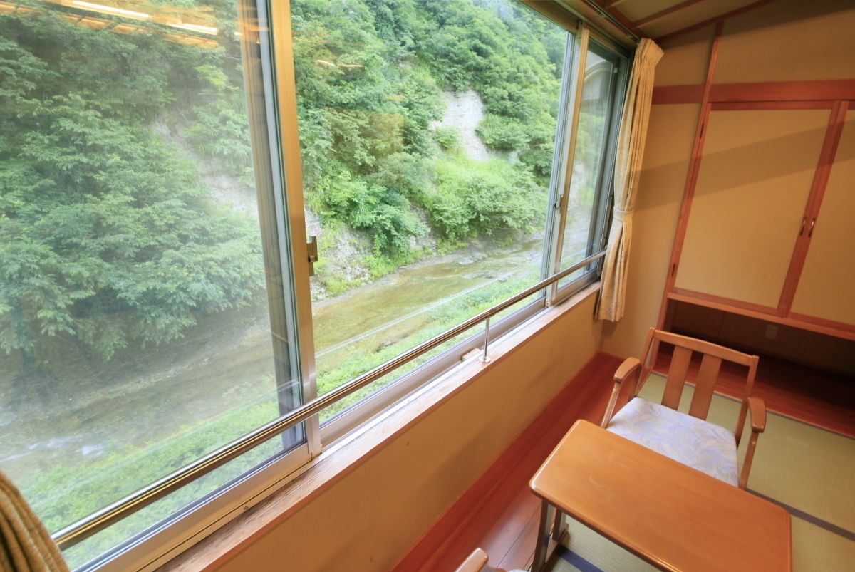 Habitación con un gran ventanal que da a un río y un bosque. Hay un banco de madera y una mesita.
