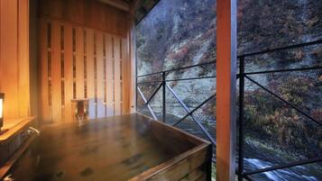 A wooden spa bath with a view of a forested hillside.