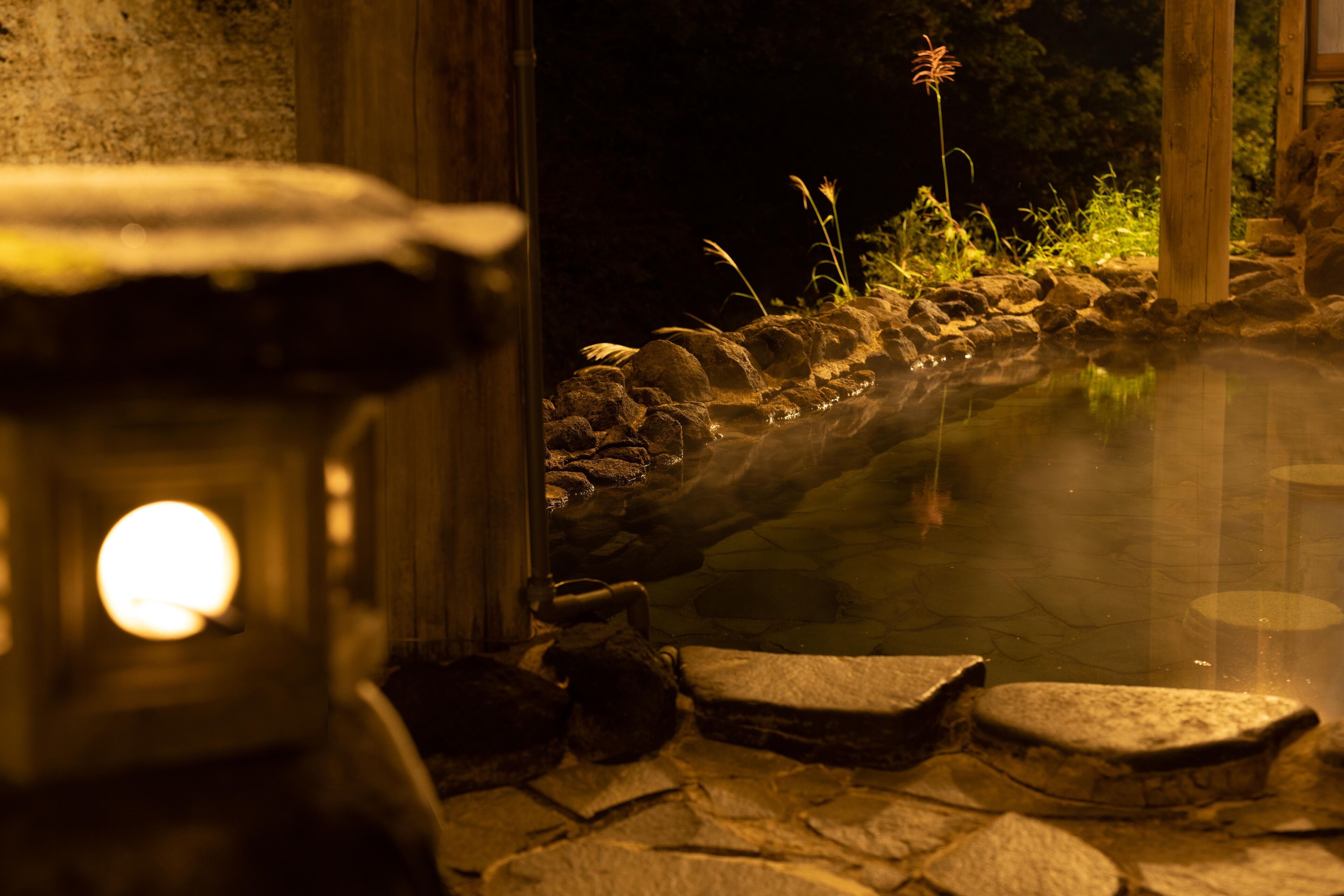 Un área de aguas termales naturales de piedra, con un farol, rocas y plantas.