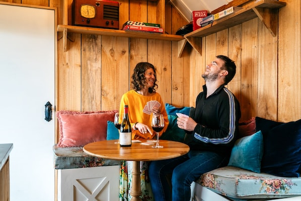 A wooden interior with a round table, a bottle of wine, and playing cards. - The Settlers Hut (Waiheke Island)