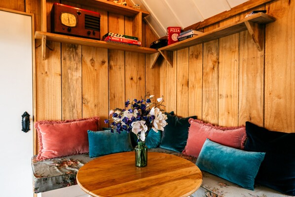 A cozy corner with a wooden bench, a round wooden table, and a vase of flowers. - The Settlers Hut (Waiheke Island)