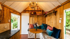 A cozy wooden interior with a bench, a table, and a chandelier. - The Settlers Hut (Waiheke Island)