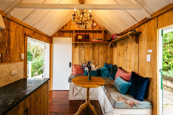 A cozy wooden interior with a bench, a table, and a chandelier. - The Settlers Hut (Waiheke Island)