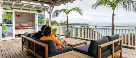 A covered outdoor seating area with wooden furniture and a view of the ocean.