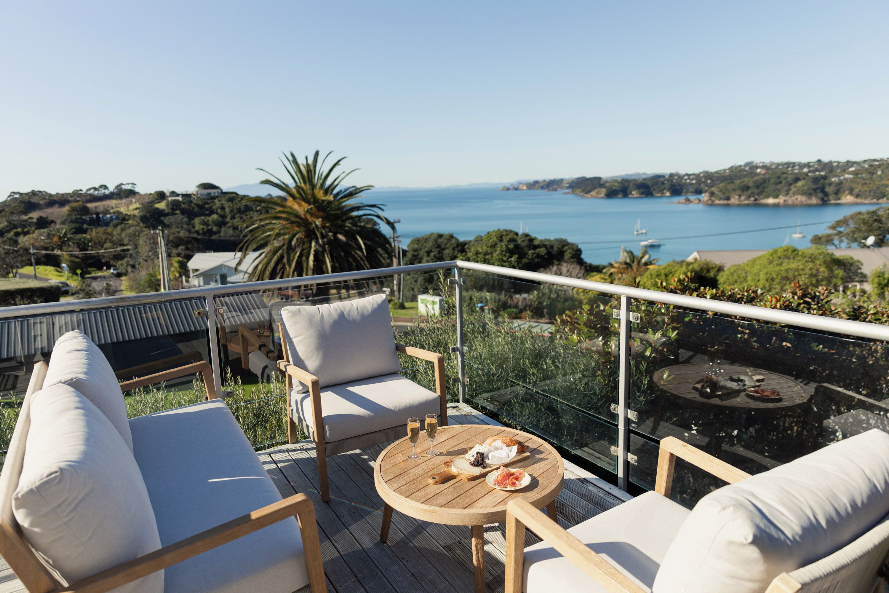 Un balcon avec vue sur la mer, aménagé avec un canapé et des fauteuils, ainsi qu’une petite table sur laquelle sont disposés de la nourriture et des boissons.