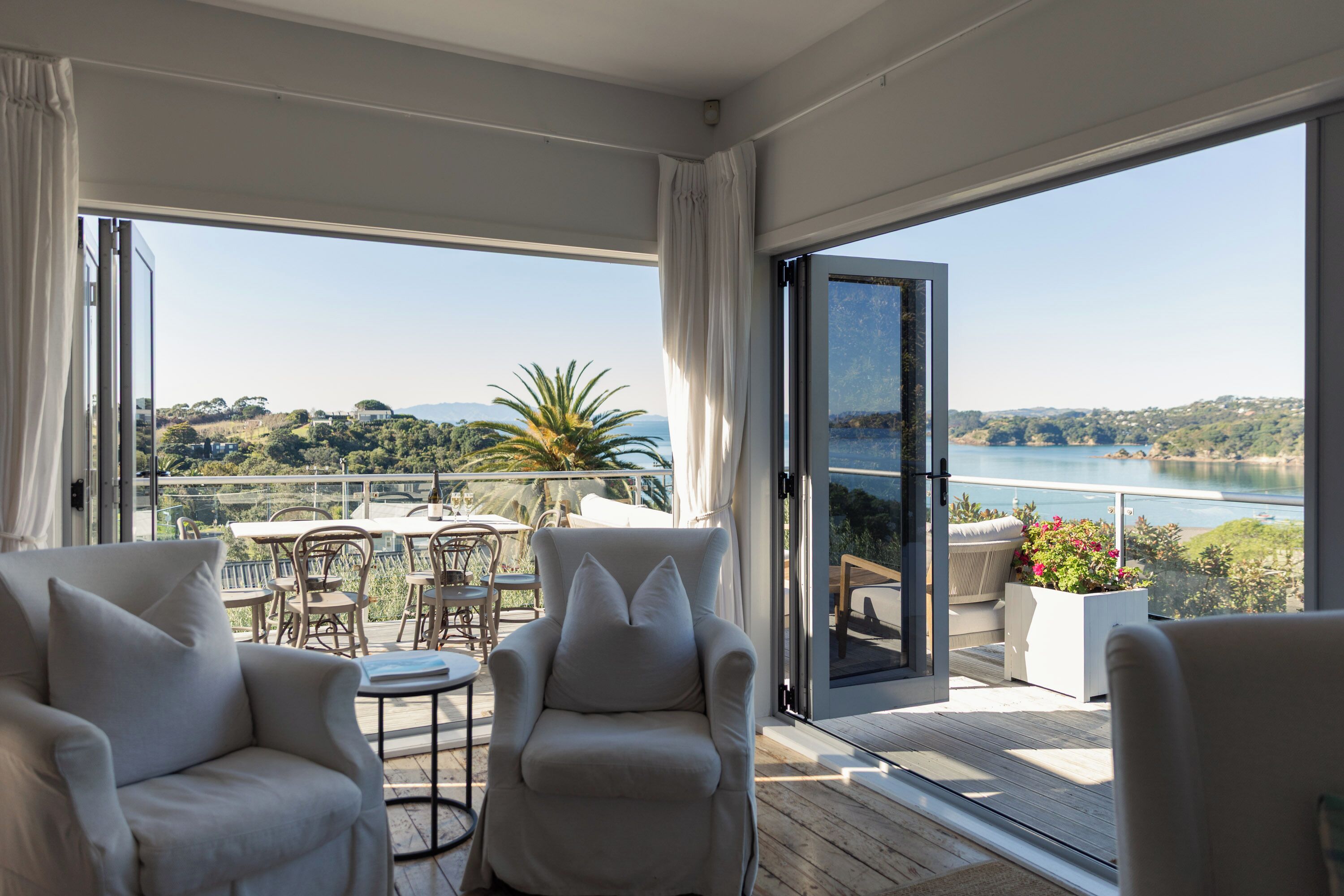 Ein Balkon mit Tisch und Stühlen, Blick auf ein Gewässer und eine Landschaft mit Bäumen und Hügeln.