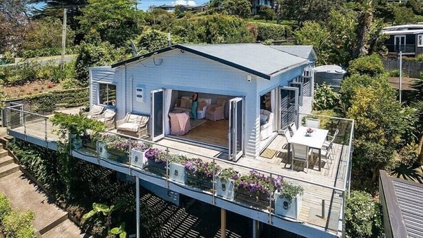 A small, single-story house with a deck and a covered outdoor seating area. - The Vintage Cottage (Waiheke Island)