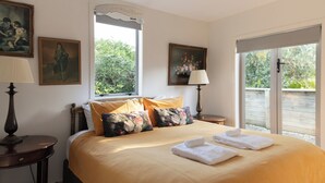 A hotel room with a bed, two nightstands, a window, and two paintings on the wall. - The Vintage Cottage (Waiheke Island)