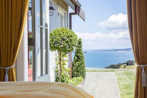Quarto com vista para o mar, janela com cortinas e uma planta no parapeito.