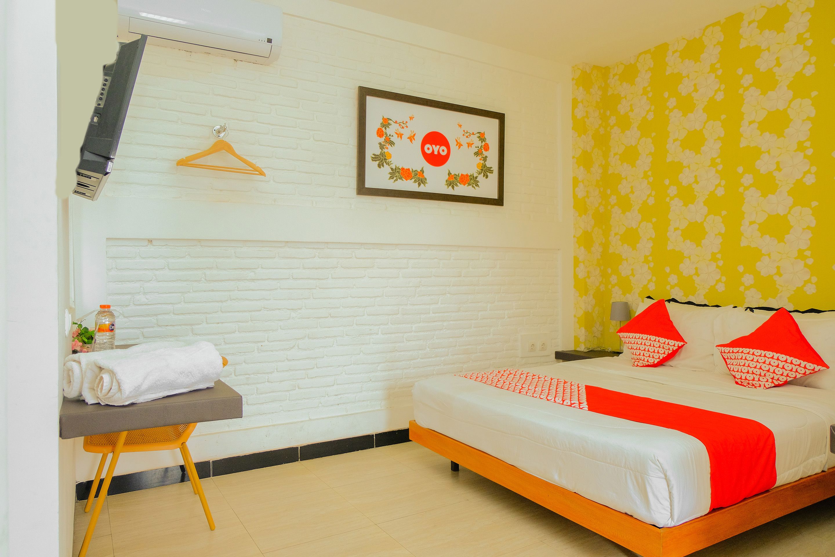 Une chambre d’hôtel avec un lit, un bureau sur lequel est posée une serviette, un tableau encadré et un mur orné d’un motif floral.