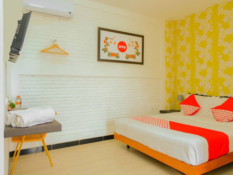 A hotel room with a bed, a desk with a towel, a framed picture, and a wall with a floral pattern.