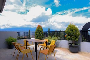 A patio with a table and chairs, potted plants, and a view of the sky and clouds. -  OYO 354 32 Guest House (Batu)