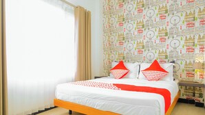 Un lit avec une literie blanche et orange, deux oreillers rouges et un papier peint à motifs représentant des bâtiments et des horloges.