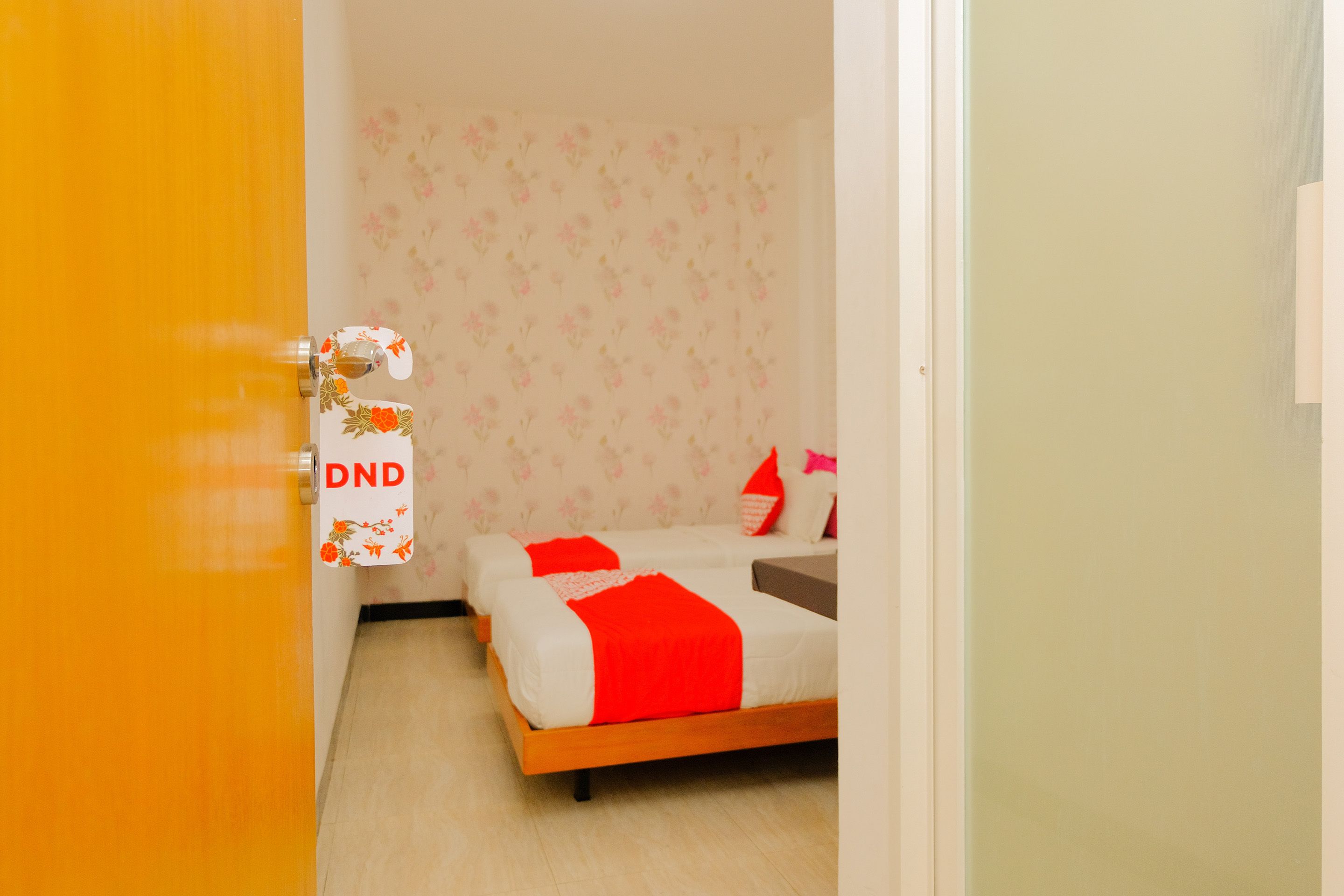 Una habitación con dos camas, una con frazada y almohadas rojas, y un cabecero de madera.