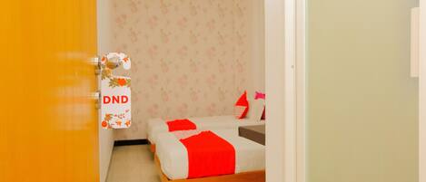 Una habitación con dos camas, una con frazada y almohadas rojas, y un cabecero de madera.