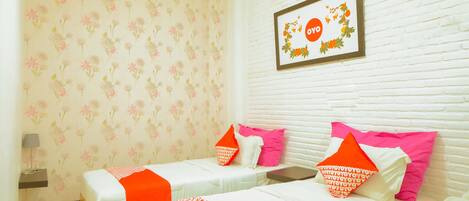 A hotel room with two beds, floral wallpaper, a framed picture on the wall, and a small bedside table with a lamp.