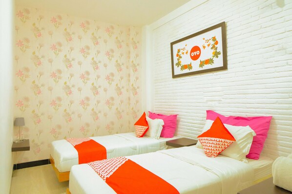 A hotel room with two beds, floral wallpaper, a framed picture on the wall, and a small bedside table with a lamp.