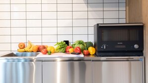 Eine Küche mit einem Edelstahlkühlschrank, einer Mikrowelle und einer Auswahl an frischem Obst und Gemüse auf der Arbeitsplatte.